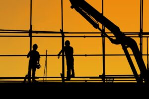Silhouette of two construction workers on scaffolding with a bright orange background.