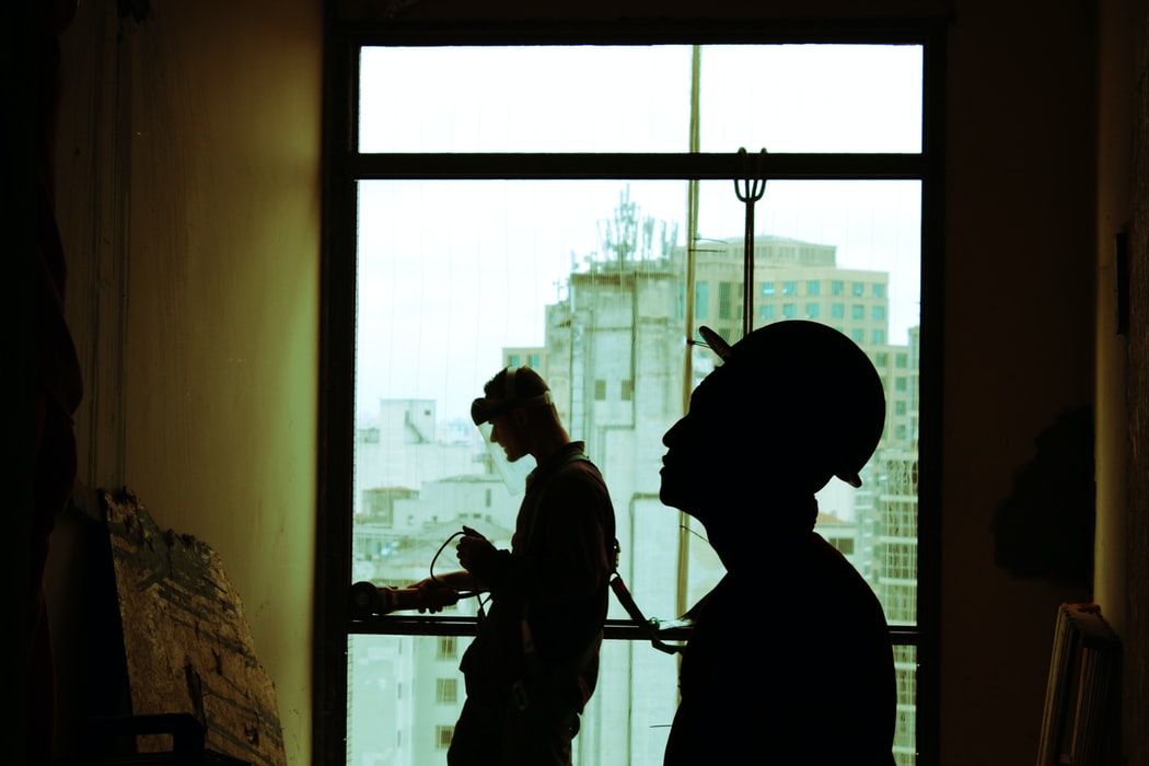 Two construction workers working inside a room with a big window.