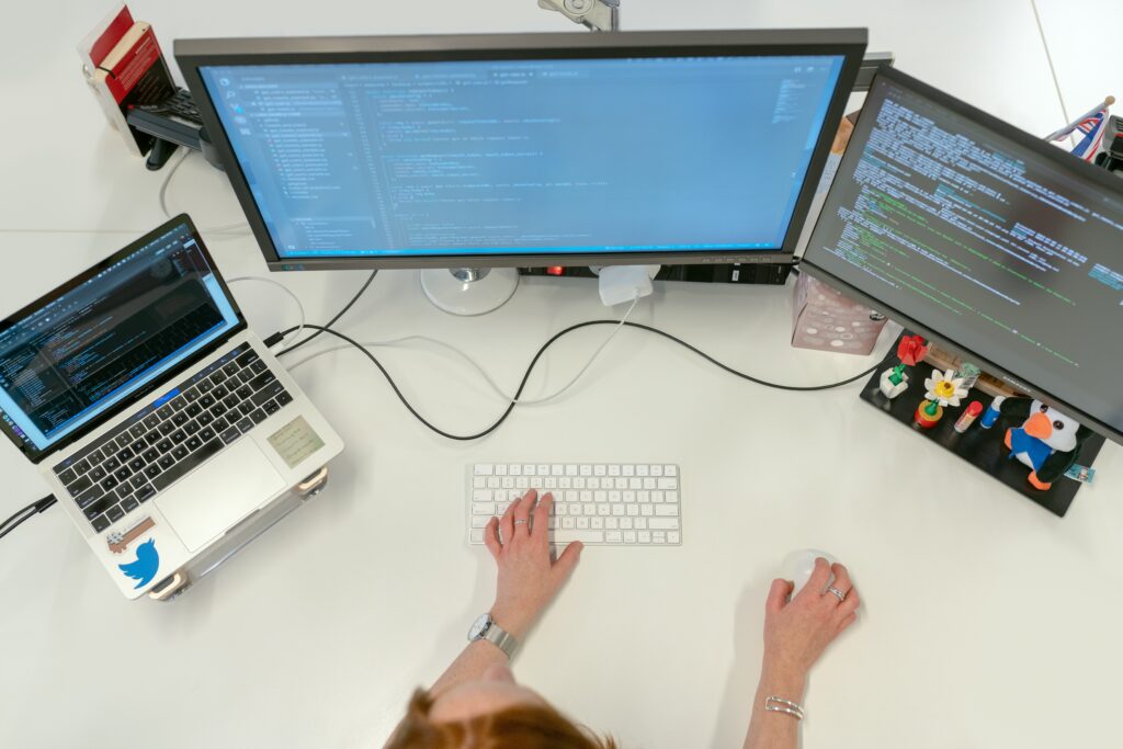 Woman using a laptop and two computer monitors to write code.